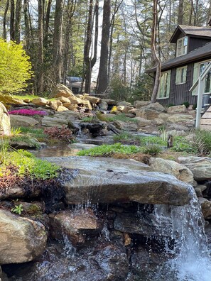 A rustic cabin with a stone waterfall feature in a forested area. - Newly renovated mountain view home in High Hampton, minutes from Cashiers, NC (Cashiers)