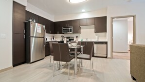 A modern kitchen with dark cabinets, stainless steel appliances, and a dining area with chairs and a table.