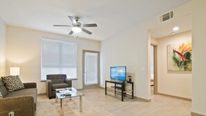 A modern living room with a ceiling fan, a flat-screen TV, a sofa, a coffee table, and a painting on the wall.