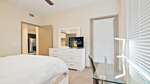 A bedroom with a bed, a dresser, a TV, and a glass table.