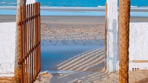 A beach entrance with a wooden gate and a sign reading "Chalís Vila Chuva".