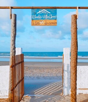 A beach entrance with a wooden gate and a sign reading "Chalís Vila Chuva". - Beachfront studio with a beautiful view of the ocean. (CE)