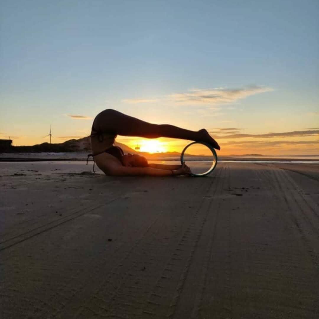 A person lying on a sandy beach at sunset, holding a hula hoop.