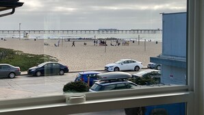 Ein Strand mit einem Pier im Hintergrund, Autos im Vordergrund und einem Rettungsturm.
