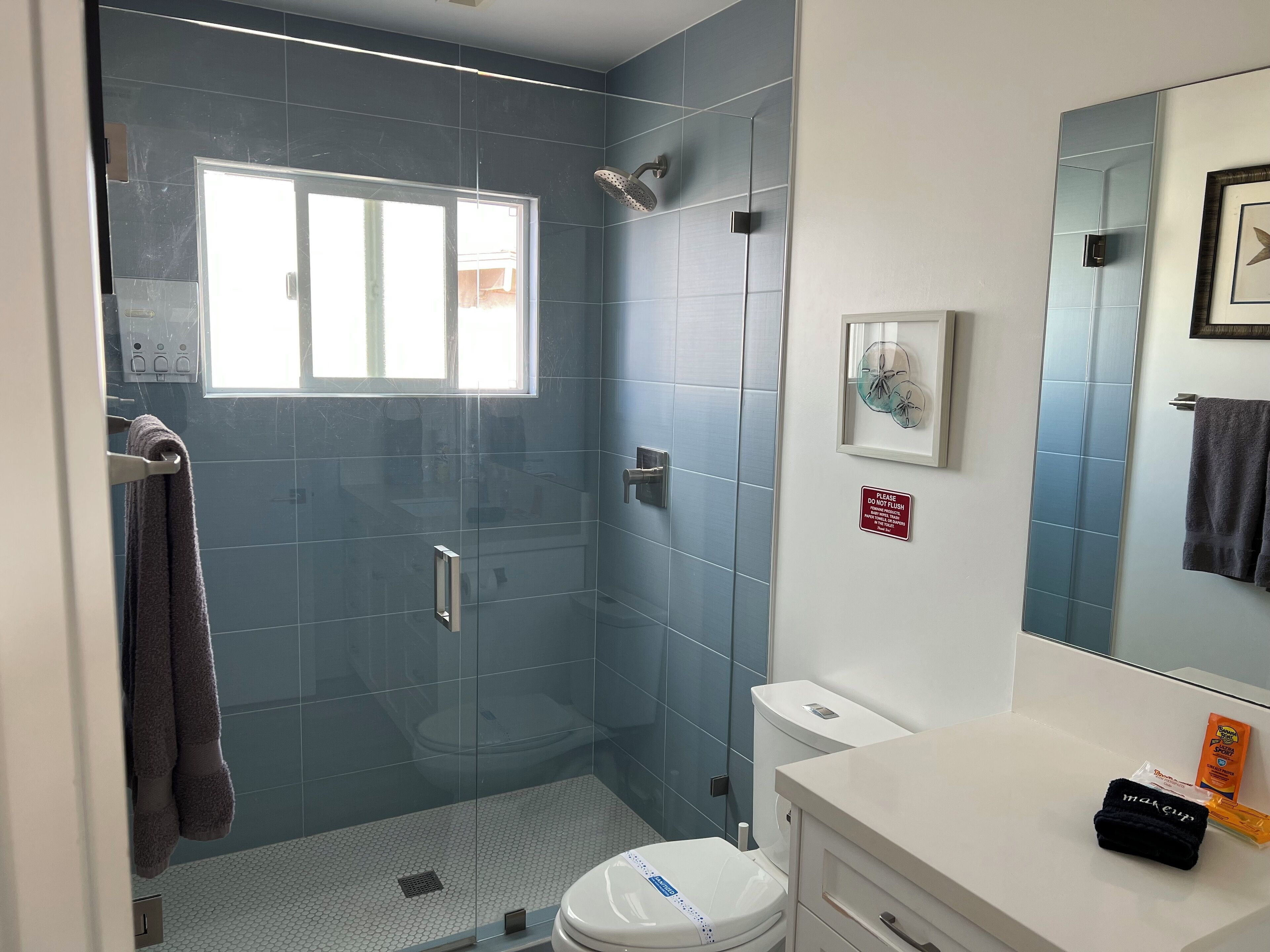 A bathroom with a glass-enclosed shower, a toilet, and a sink with a towel and toiletries.