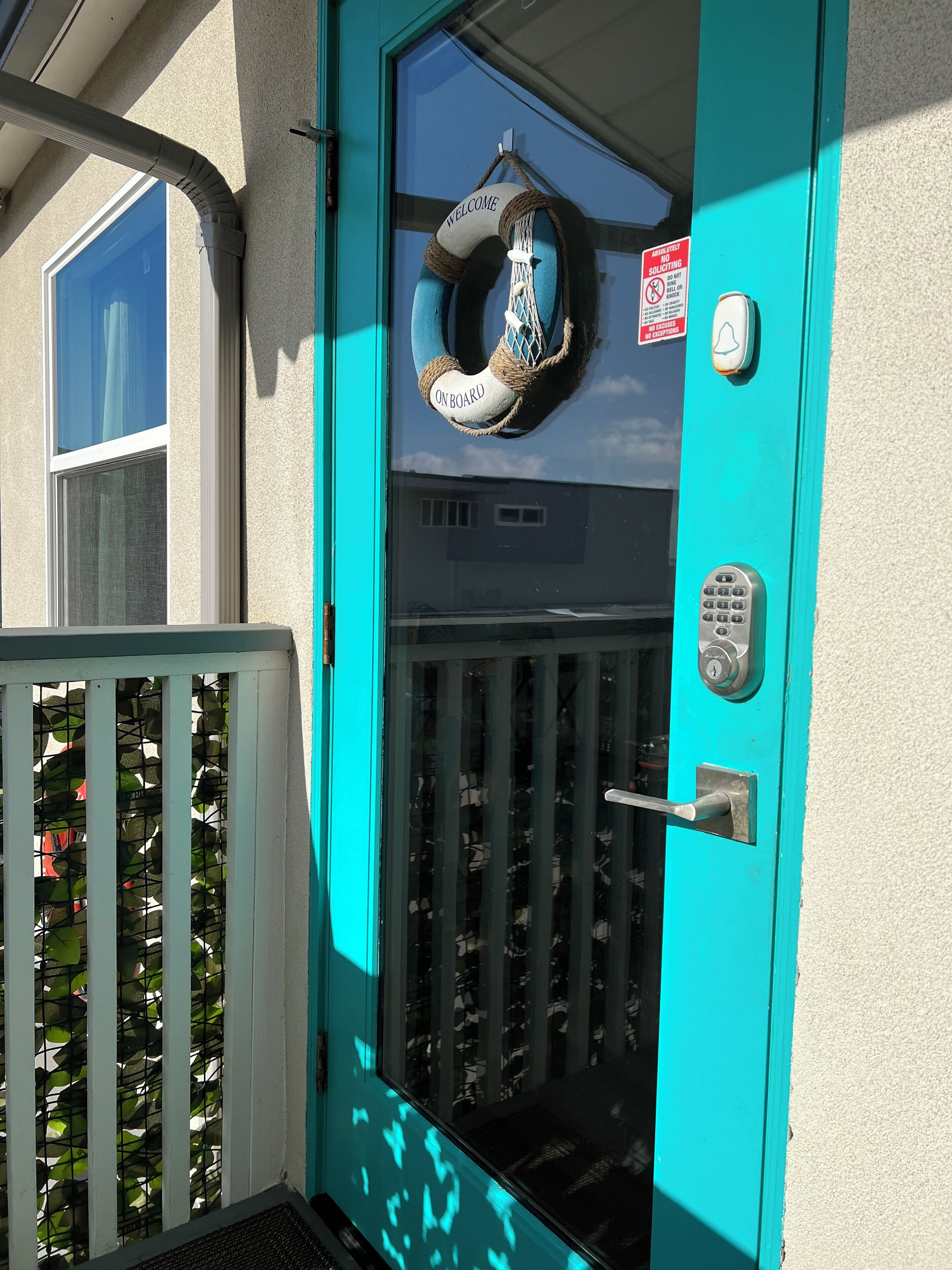 A turquoise door with a welcome sign, a keypad, and a doorbell.
