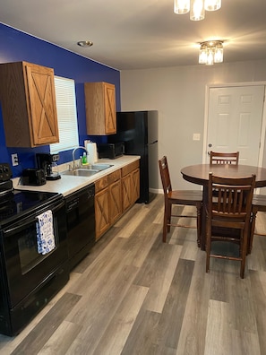 Enjoy meals in this kitchen with a dining table and chairs, featuring a refrigerator and a door leading to more space.