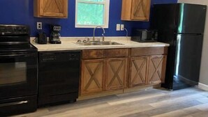 A kitchen with blue walls, wooden cabinets, a black refrigerator, and a window. - Barn and bling on Windrock (Oliver Springs)