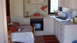 A compact kitchen with white cabinets, a stove, and a sink. There is a clock on the wall and a window providing natural light. - Country house (Pula)