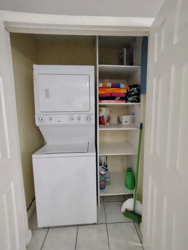 A laundry area with a washing machine and dryer, shelves with folded clothes, and a mop.