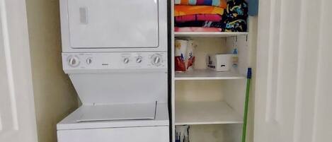 A laundry area with a washing machine and dryer, shelves with folded clothes, and a mop.