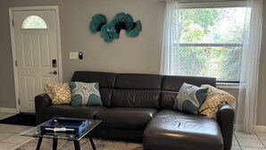 Ein Wohnzimmer mit braunem Ledersofa, einem Glastisch und Wanddekoration.