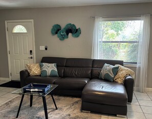 A living room with a brown leather sofa, a glass coffee table, and decorative wall art.
