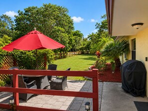 Un patio con mobiliario exterior, un paraguas rojo y césped.