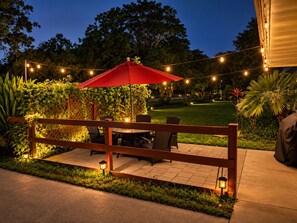 An outdoor patio with a wooden fence, a red umbrella, and string lights.