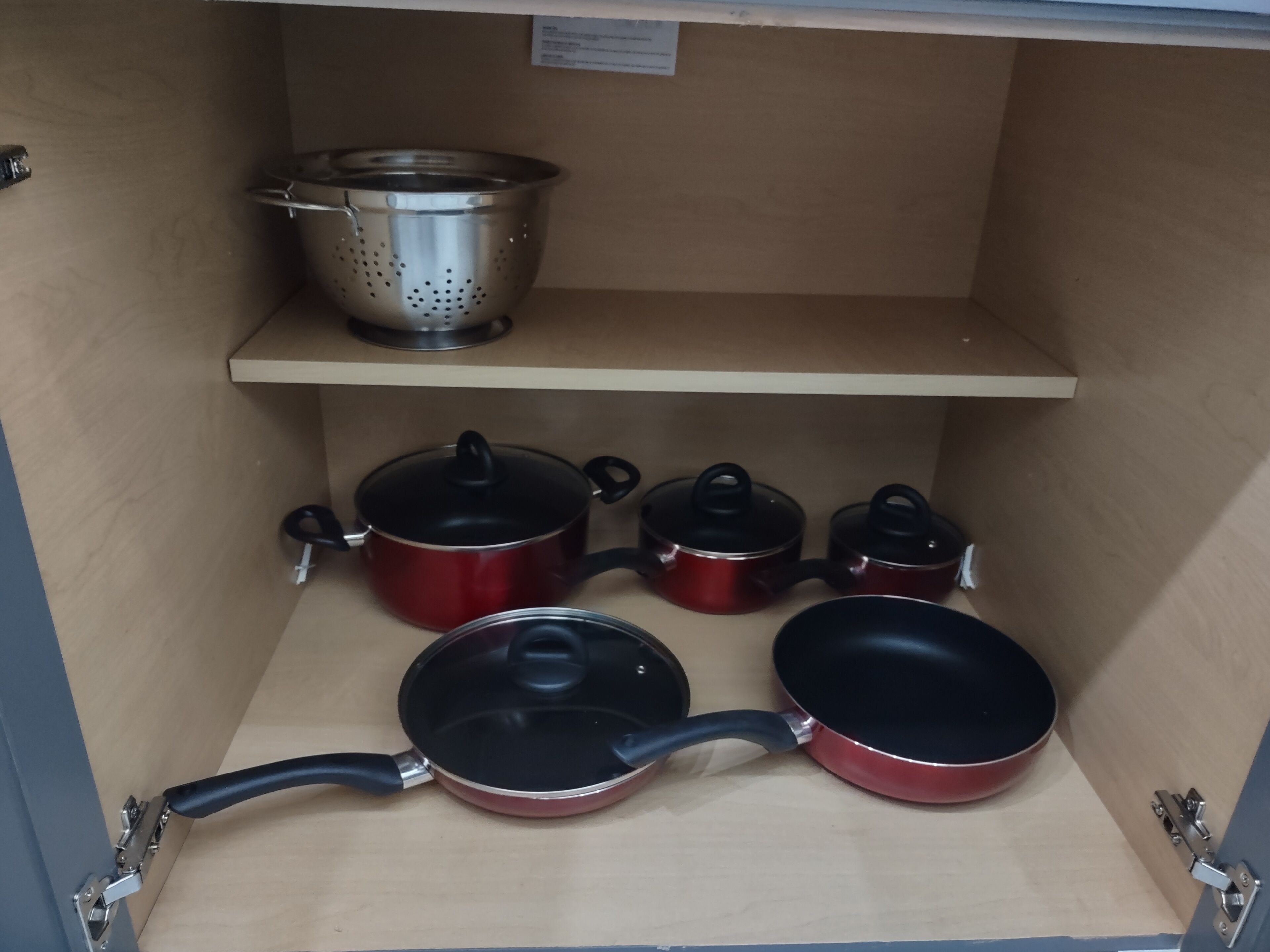 A kitchen cabinet with pots, pans, and a colander.