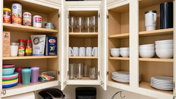 A kitchen with open cabinets displaying various food items, cookware, and glassware.