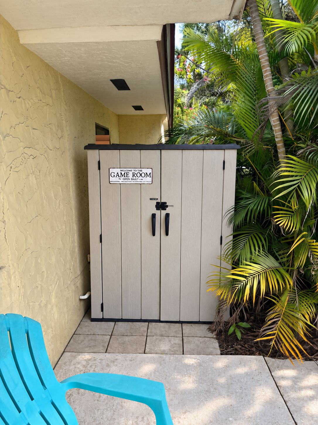 A game room with a sign, a blue chair, and tropical plants.