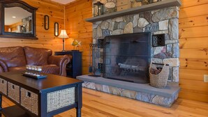 A cozy living room with a stone fireplace, leather sofa, and a coffee table. - Maple Cove Lodge on Lake Sebago Waterfront! (Casco)