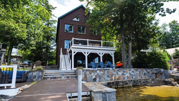 A cabin with a balcony and outdoor seating area, surrounded by trees and a small pond. - Maple Cove Lodge on Lake Sebago Waterfront! (Casco)