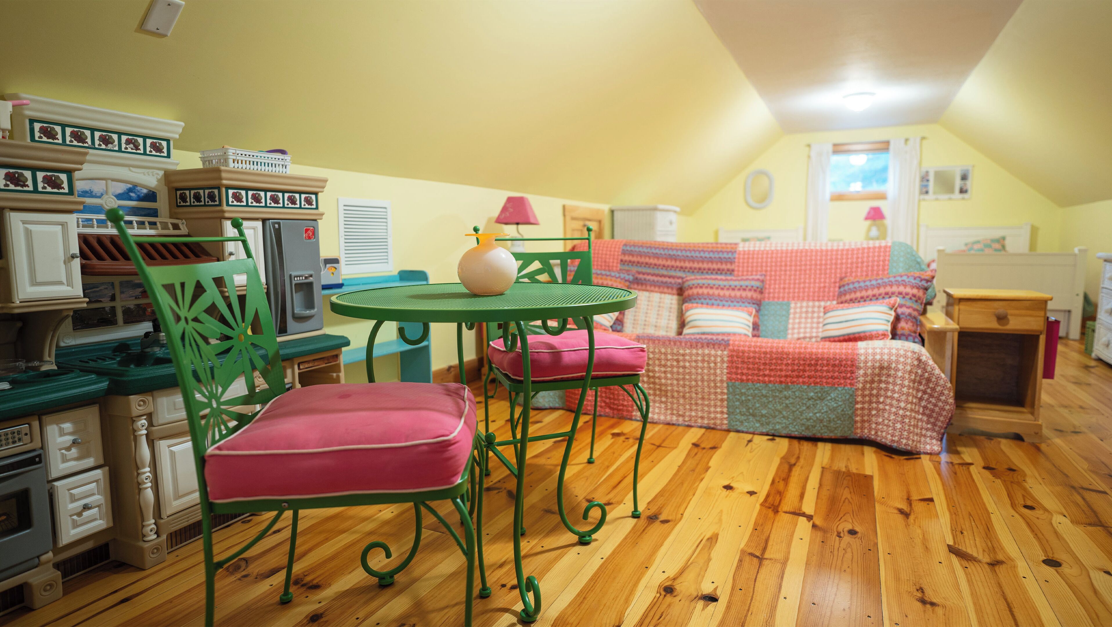 A cozy room with a wooden floor, a green metal table, a red cushioned chair, and a colorful sofa.