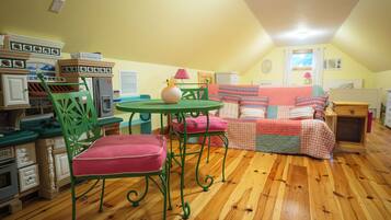 A cozy room with a wooden floor, a green metal table, a red cushioned chair, and a colorful sofa.