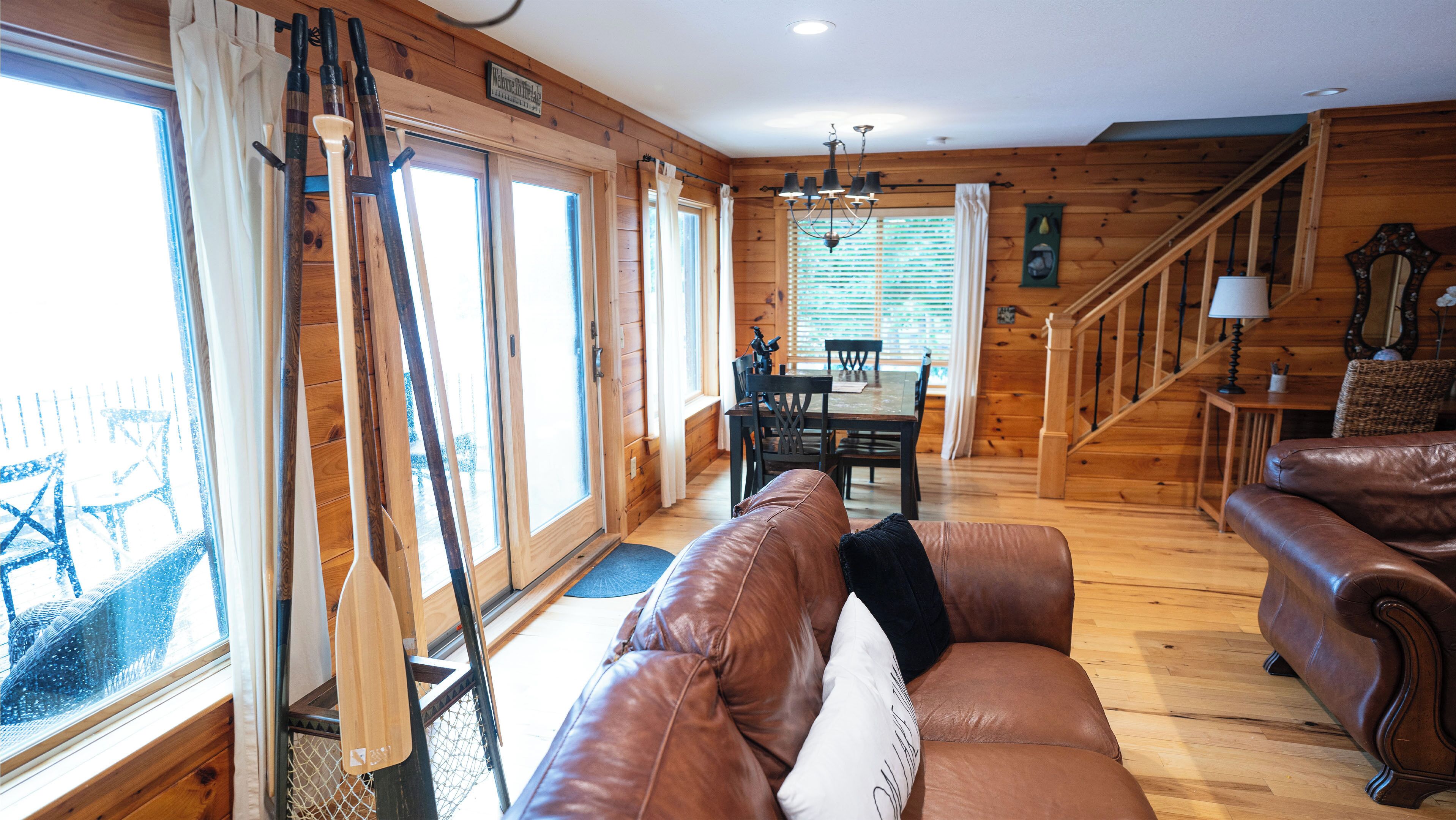 A cozy cabin interior with a wooden floor, a leather sofa, a dining table, and a staircase.
