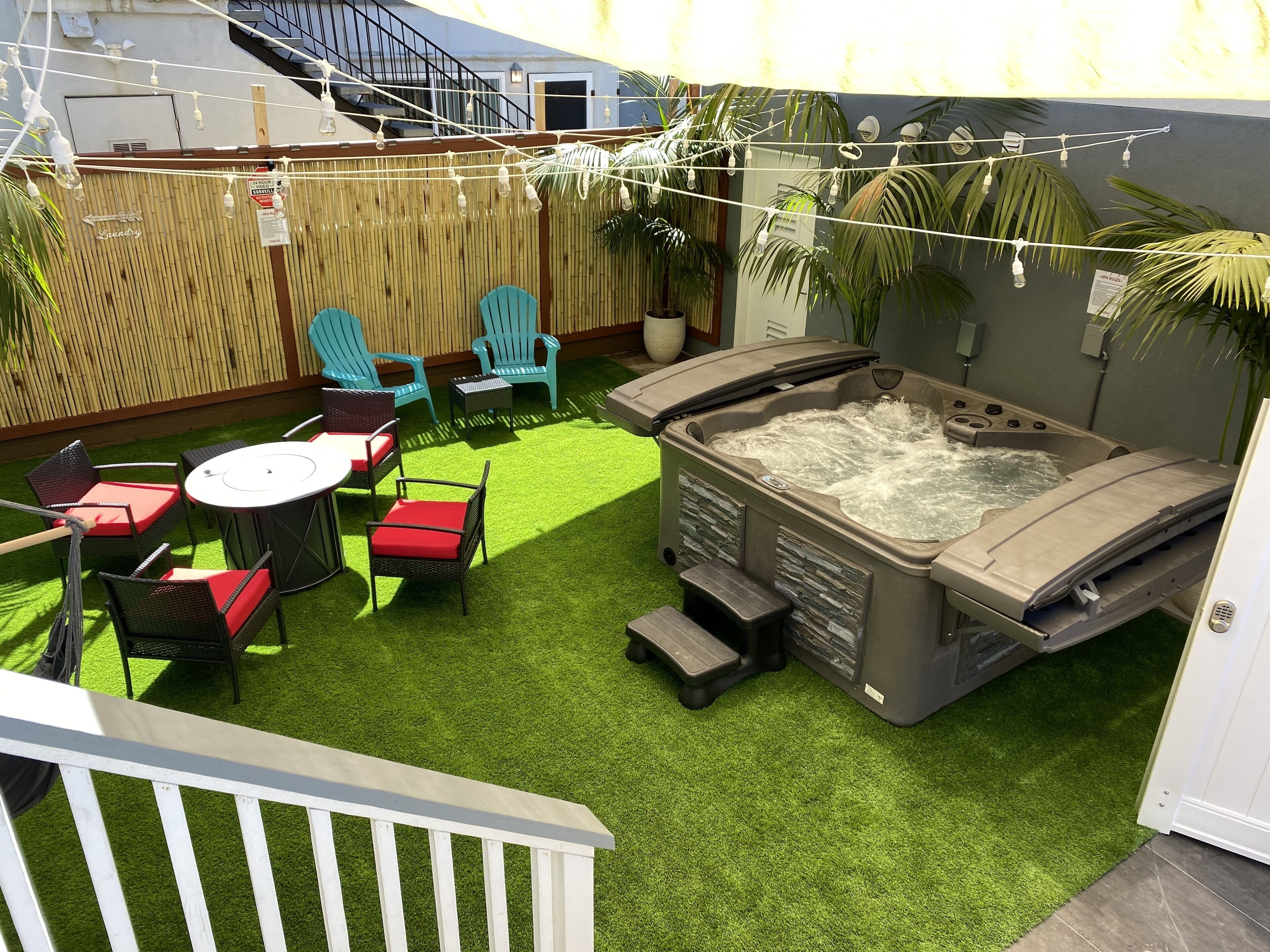 A backyard with artificial grass, a hot tub, outdoor furniture, and string lights.