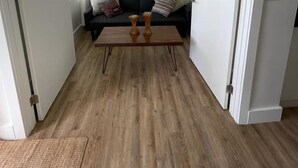 Ein modernes Wohnzimmer mit einer schwarzen Couch, zwei Holztischen und einem hellen Boden.