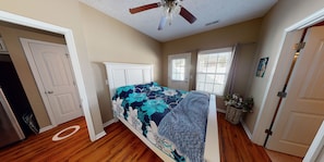 A bedroom with a bed, a ceiling fan, a window with blinds, and a door.