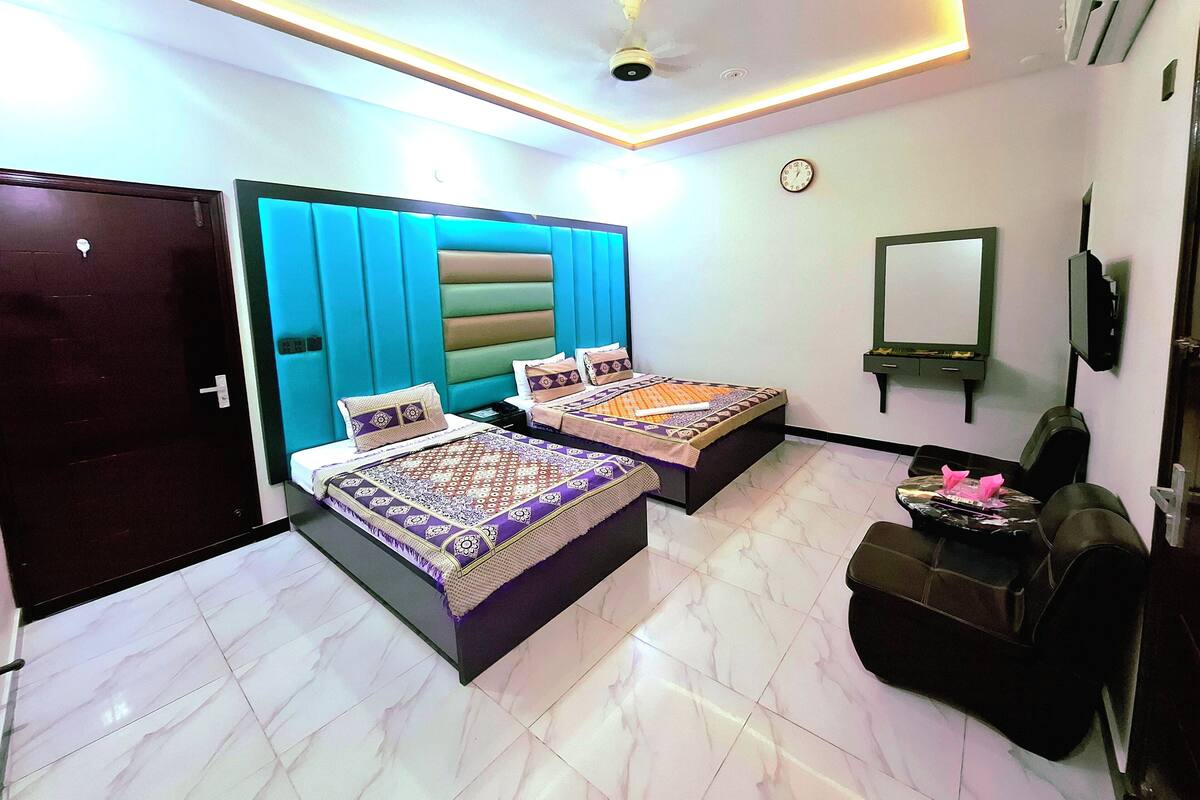 A hotel room with two beds, a ceiling fan, a clock, a TV, and a door.