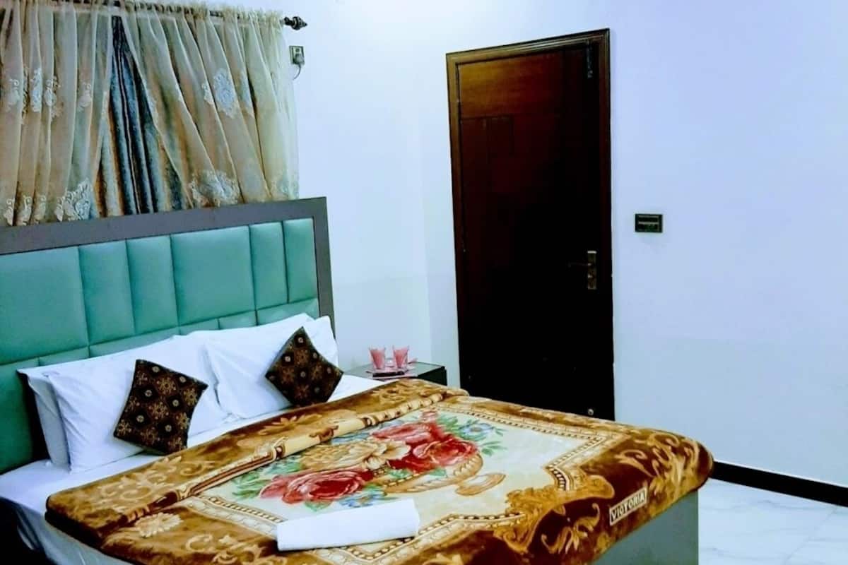 A hotel room with a bed, a nightstand, a wall-mounted air conditioner, and a door.