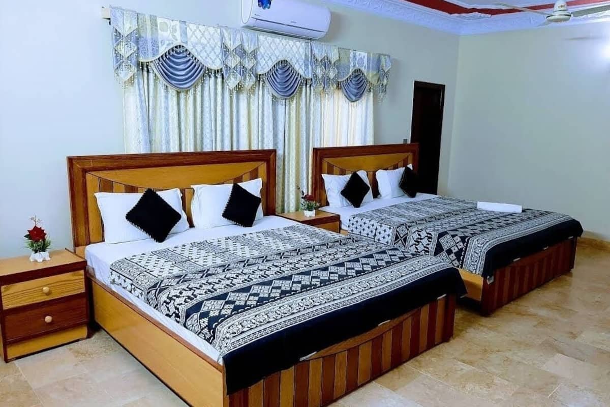 A double bed with a patterned bedspread, a nightstand with a lamp, and a window with decorative curtains.