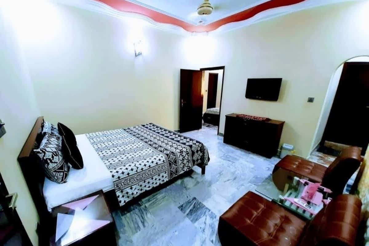 A bedroom with a bed, a TV, a dresser, and a seating area.