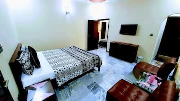 Un dormitorio con cama, televisor, cómoda y una zona de estar.