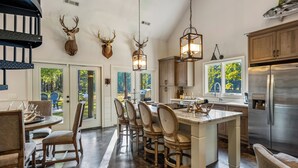 A spacious kitchen with a central island, wooden cabinets, and a stainless steel refrigerator. - Woodland Gameday Getaway Near Tuscaloosa – Pond Views, Pavilion, Firepits & More (Akron)
