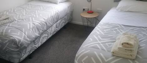 Habitación de hotel con dos camas, una mesita de noche con lámpara y una ventana con cortinas.