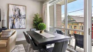 A modern room with a dining table, chairs, a potted plant, and a large window offering a view of buildings outside. - New Luxurious & Beautiful! - 2br/2ba w/ Pool! (New Orleans)