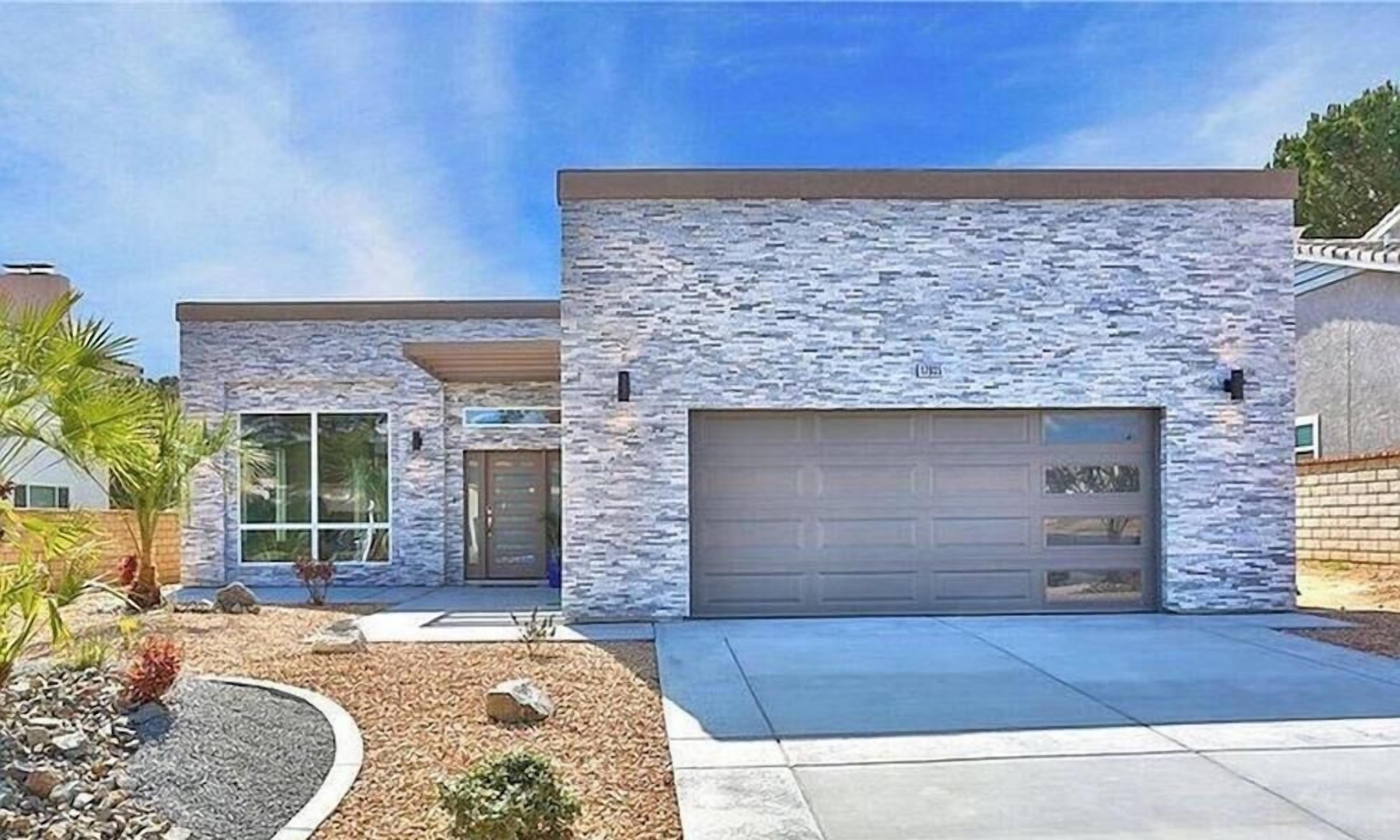 A modern two-story house with a stone facade, a garage, and a landscaped front yard with rocks and plants.