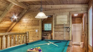 A wooden pool table in a room with wooden walls and a sloped ceiling.