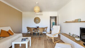 A modern living room with a sofa, a coffee table, a dining area with wicker chairs, a white armchair, and a fireplace. - Appartement Provenza - Welkeys (Saint-Cyr-sur-Mer)