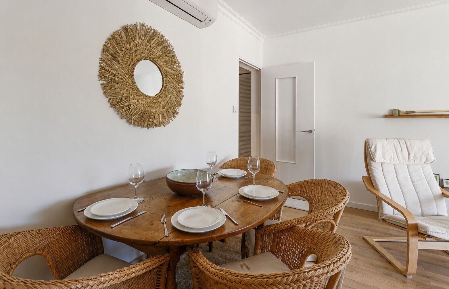 Un coin repas avec une table ronde en bois, des chaises en osier et un miroir décoratif accroché au mur.