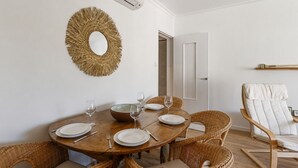 A dining area with a round wooden table, wicker chairs, and a decorative mirror on the wall. - Appartement Provenza - Welkeys (Saint-Cyr-sur-Mer)