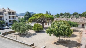 A courtyard with a large tree, a stone wall, and a building with a tiled roof. - Appartement Provenza - Welkeys (Saint-Cyr-sur-Mer)
