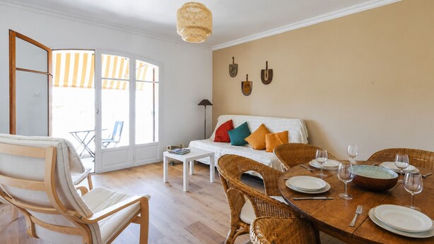 A dining area with a round wooden table set for four, surrounded by wicker chairs. - Appartement Provenza - Welkeys (Saint-Cyr-sur-Mer)