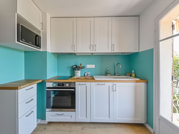 A compact kitchen with white cabinets, a microwave, an oven, a sink, and a window with a view of greenery.