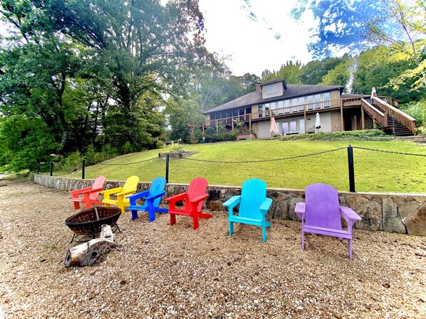 A row of colorful Adirondack chairs on a gravel path with a stone wall, leading to a building with a wooden deck and stairs.