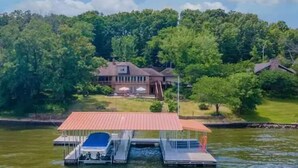 Una propiedad junto al lago con muelle, piscina y una casa grande rodeada de árboles frondosos.