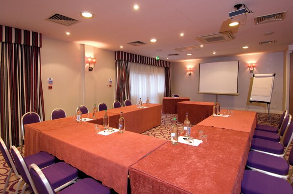 A conference room with a large oval table, purple chairs, and a whiteboard. - Premier Inn München City Zentrum (Munich)