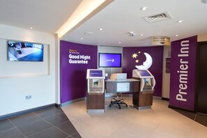 A hotel reception area with a check-in counter, a television displaying a room view, and a sign indicating a 'Good Night Guarantee.' - Premier Inn Portsmouth Havant South (Havant)